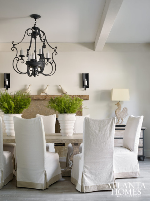 In the dining room, texture in the form of limewashed floors, a rough-hewn mantel and a light elm pedestal dining table and slipcovered chairs, both from Bungalow Classic, complicate the play on light. Carved rooster lamp from Parc Monceau.