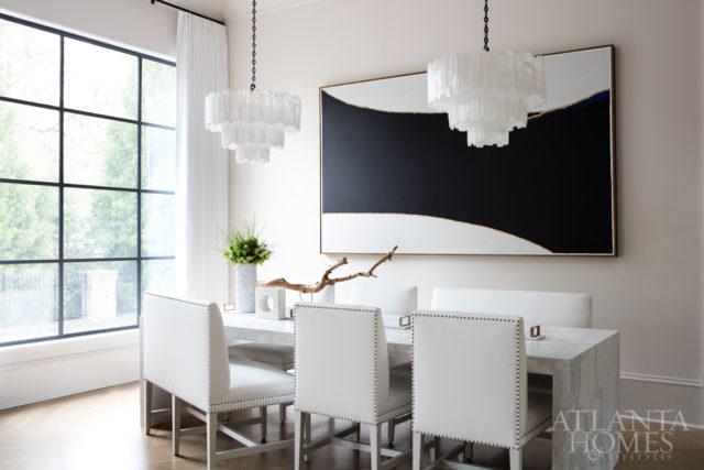 Because the breakfast room is open to the kitchen, Broaddus commissioned a waterfall-edge table from Miami Circle Marble to match the island. The painting by Lynn Raney was one of the many new pieces of art she helped the young homeowners secure to begin their art collection. The pair of selenite chandeliers are by Ron Dier through Jerry Pair, and the new steel window is by Forge Fine Steel.