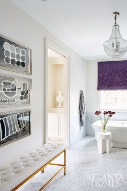 In the master bathroom, contemporary features, such as an Irish monochromatic watercolor set from B.D. Jeffries and gray painted wood vanity mirrors from South of Market, complement traditional elements, including Carrara marble tile and a tufted Sylvia bench from B.D. Jeffries.