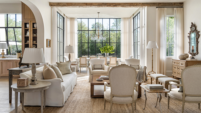 Read article: This Serene Trilith New Build Proves Great Design Is a Team Effort Living room with white sofa, armchairs, and dining area visible through large windows.