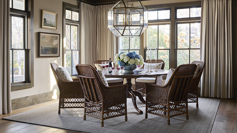 Read article: How a Milton Home Renovation Brought Timeless English Country Style to Life Dining room with wicker chairs, round table set for dinner, and large geometric chandelier.