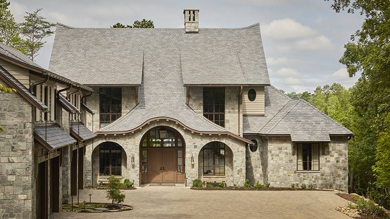 Read article: This Lake Keowee Home Brings a Taste of British Sensibility Down South Stone house with arched entryway, multiple gables, and dormer windows.