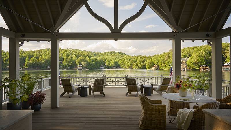 Read article: A Respected Design Team Crafts the Ultimate Lake Burton Family Retreat Covered porch with wicker chairs and table overlooking a lake and wooded hills