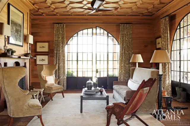 Living room with wood paneled walls and ceiling, large arched windows, velvet wingback chairs, a sofa, and a coffee table.