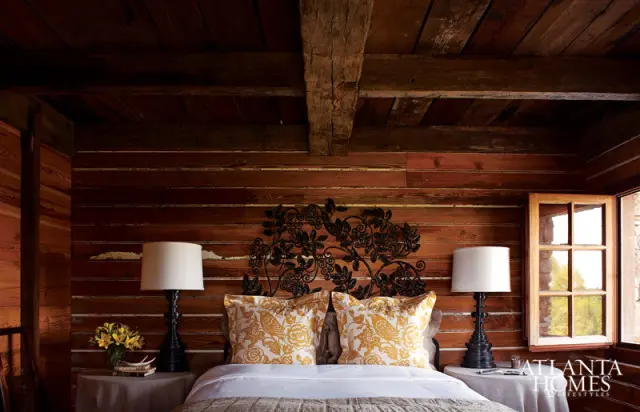 Bedroom with wood-paneled walls and ceiling, a metal floral headboard, yellow floral pillows, and two white lamps on bedside tables.