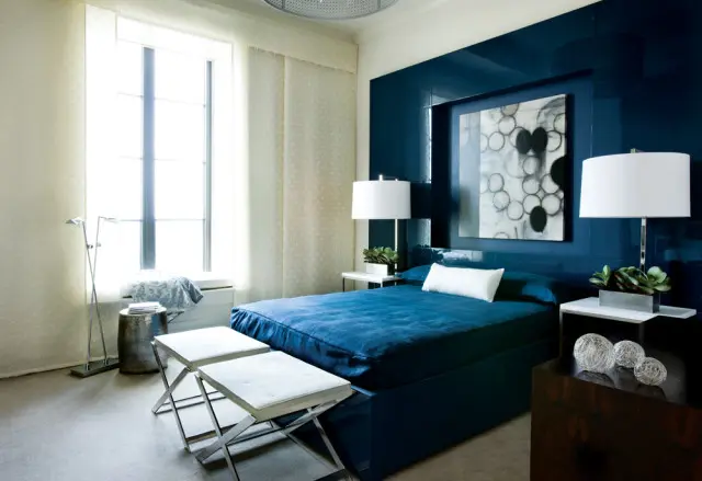 Bedroom with a large navy blue upholstered bed, a high-gloss navy blue wall panel, and a window with sheer curtains.
