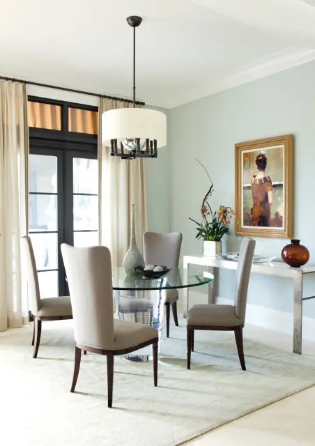 Dining room with a glass-top round table, four upholstered chairs, a console table with artwork, and a drum pendant light.