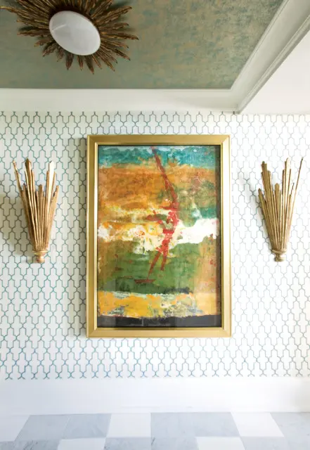 Hallway with teal and gold textured ceiling, geometric patterned wallpaper, abstract painting in gold frame, and gold sunburst sconces.