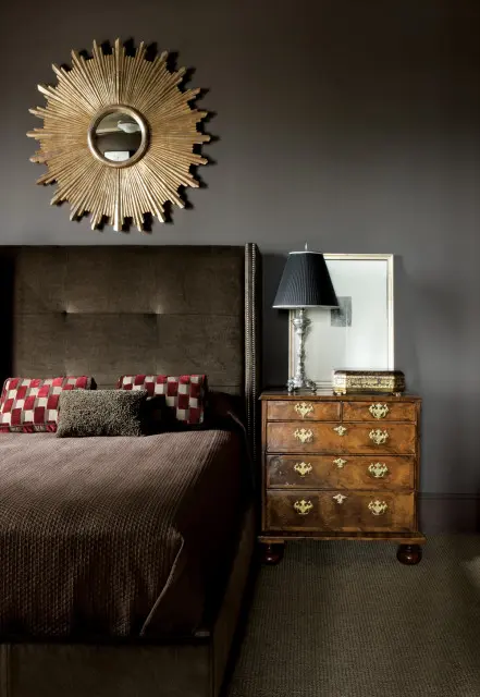 Bedroom with a tufted brown headboard, gold sunburst mirror, and a vintage wooden dresser with brass hardware.