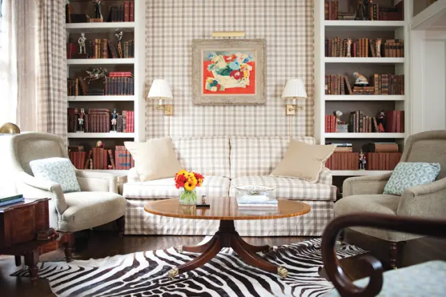 Living room with beige and white gingham sofa and chairs, flanked by bookshelves filled with books and decorative objects. A round wooden coffee table sits on a zebra print rug.