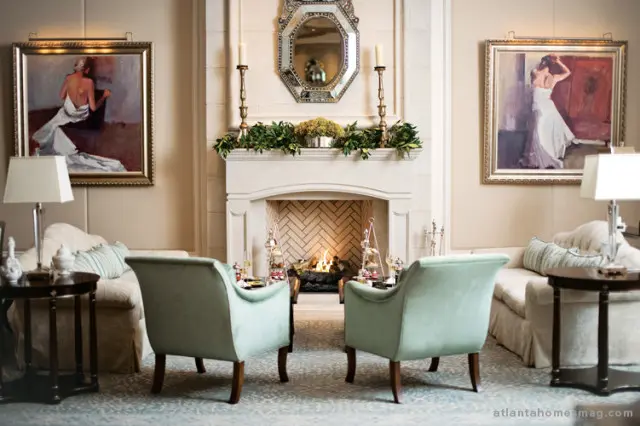 Living room with a fireplace, two light blue armchairs, and sofas. Two paintings hang on the wall flanking the fireplace.