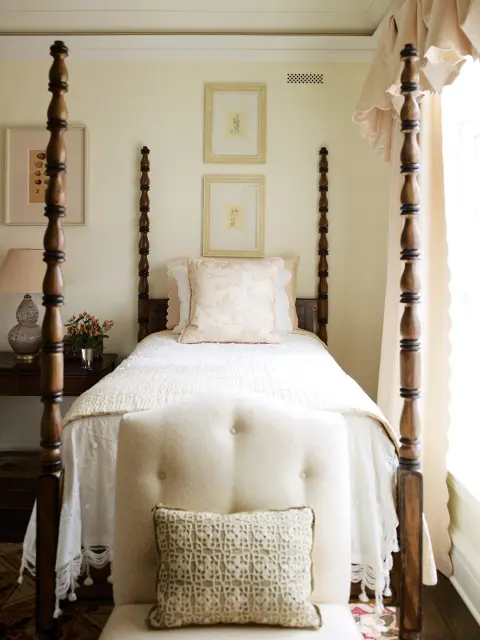 Bedroom with a dark wood four-poster bed, white bedding, and two framed botanical prints on a cream wall.
