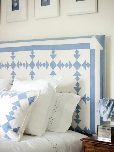 Bedroom with a white and blue geometric quilt headboard, white bedding with blue polka dots, and framed artwork on the wall.