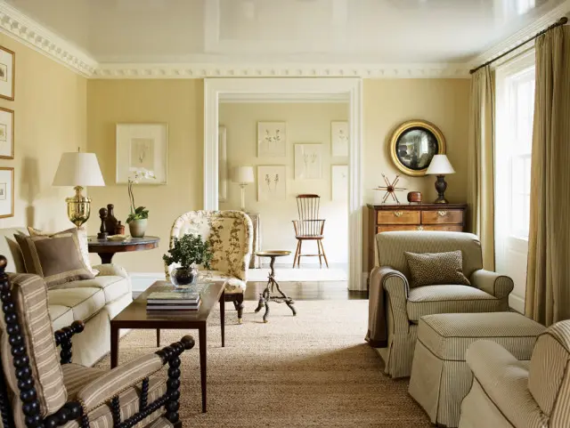 Living room with pale yellow walls, neutral jute rug, and upholstered furniture including a sofa, armchairs, and ottoman. Botanical prints hang on the walls.
