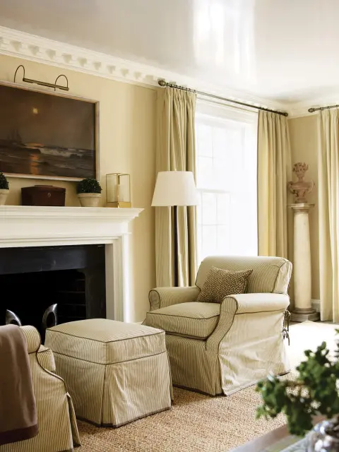 Living room with a fireplace, a striped armchair and ottoman, and a painting of a sailboat at sea above the mantel.