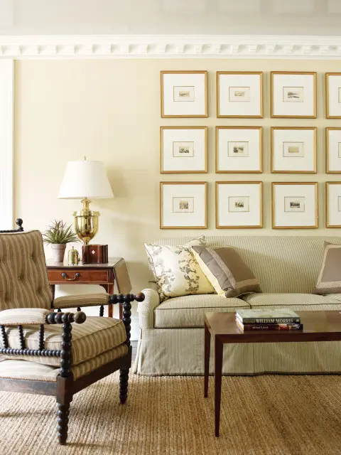 Living room with a striped sofa, tufted armchair with turned wood legs, and a wall of framed landscape prints above a jute rug.