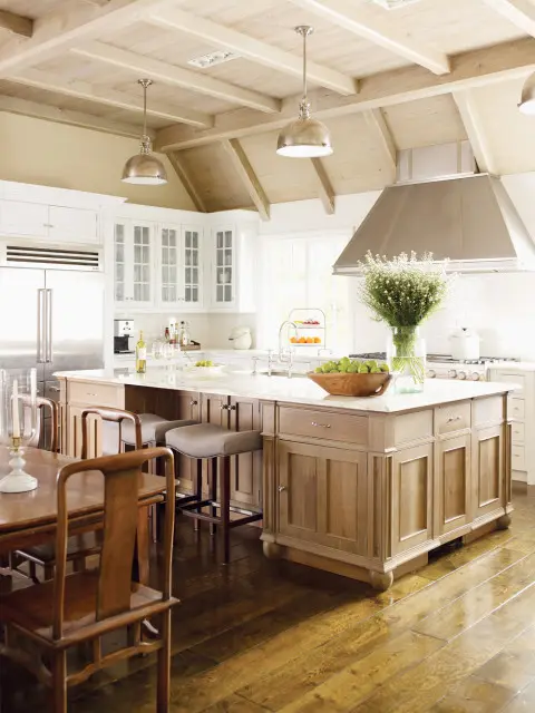 Kitchen with a vaulted, wood-beamed ceiling, white custom cabinetry, a large wood island with a marble countertop, and a stainless steel range hood.