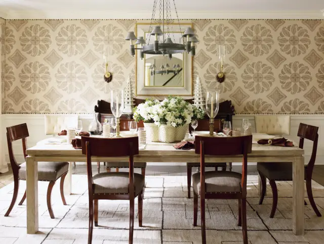 Dining room with a light wood table set for a meal, upholstered chairs, and patterned wallpaper.