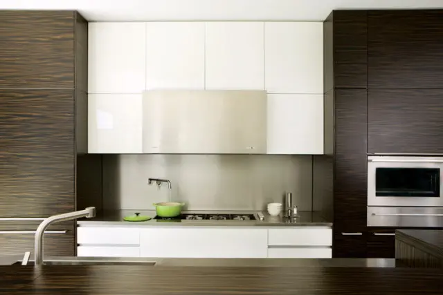 Modern kitchen with dark wood grain cabinetry, white high-gloss upper cabinets, stainless steel backsplash, range hood, and built-in oven. A green pot sits on the gas stovetop.