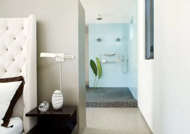 Bedroom with tufted headboard and bedside table next to a walk-in shower with light blue tile and pebble floor