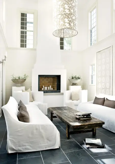 Spacious living room with white slipcovered sofas, a large white fireplace, a rustic wooden coffee table, and a tall drum pendant light with a leaf pattern.