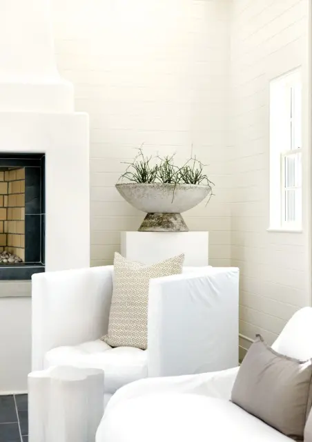 Living room with white slipcovered sofas, a modern white fireplace, and a large concrete planter with greenery.
