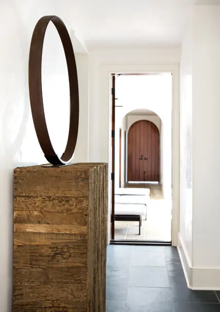 Hallway with white walls, dark slate tile floor, and a rustic wooden pedestal topped with a large metal ring sculpture.