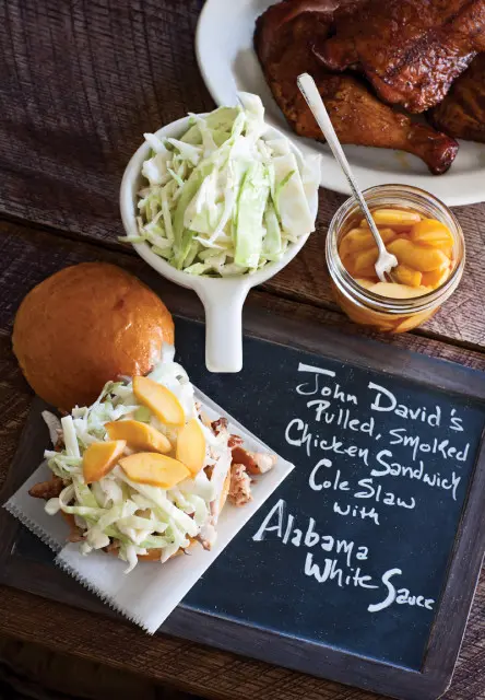 John David's Pulled, Smoked Chicken Sandwich with Cole Slaw and Alabama White Sauce, served with a side of coleslaw and pickled peaches.