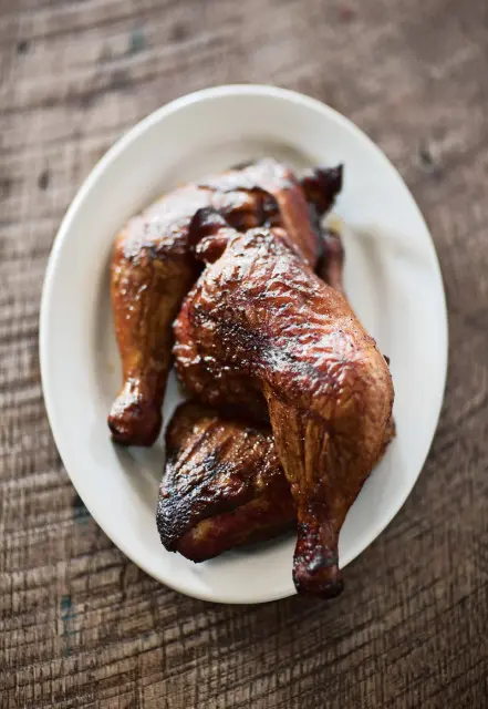Close-up of roasted chicken quarters on a white plate, with a dark wood background.