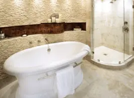 Oval freestanding bathtub with chrome fixtures next to a glass-enclosed shower with marble tile walls and floor.