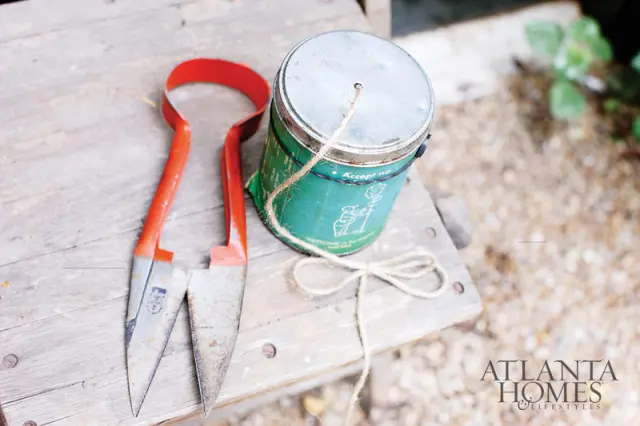 Vintage sheep shears with red handles and a green metal tin with twine tied in a bow on a weathered wooden surface.