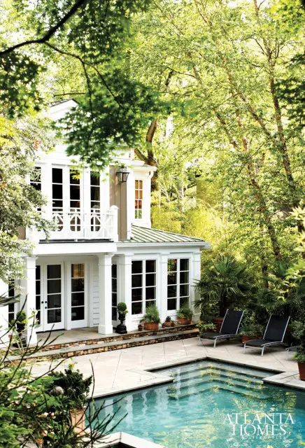 White house with green metal roof, French doors, and large windows overlooking a swimming pool and patio with lounge chairs.