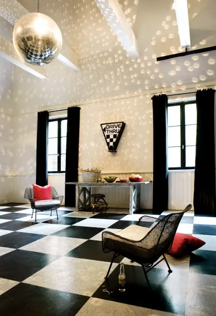 Black and white checkered floor with a disco ball hanging from the ceiling, two metal chairs with red pillows, and a table with snacks.