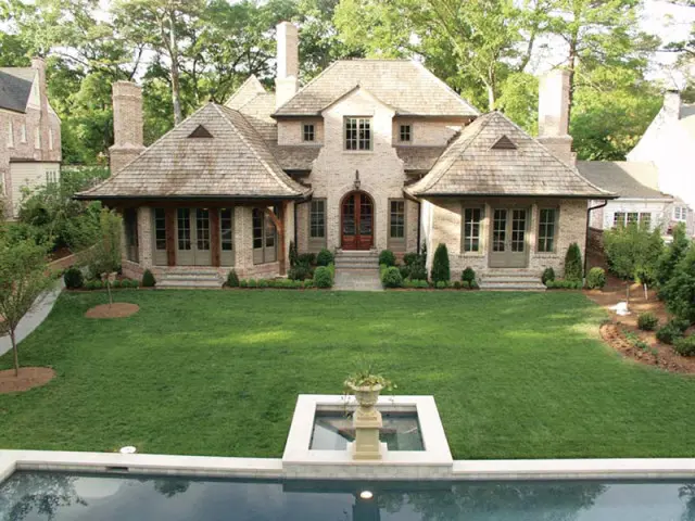 French-inspired brick residence with multi-gabled cedar shake roof, large manicured lawn, and swimming pool.