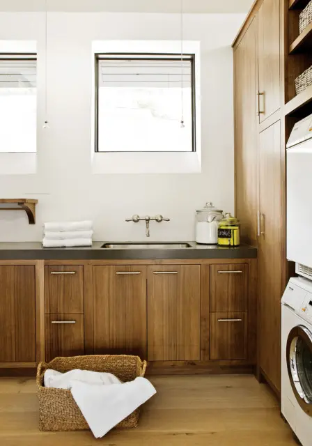 Laundry room with dark wood cabinetry, a stainless steel sink, stacked white washer and dryer, and a woven basket of white linens.
