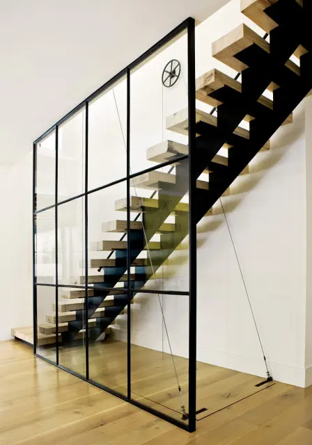Modern floating staircase with light wood treads and black metal stringers, enclosed by a glass partition with black metal grid