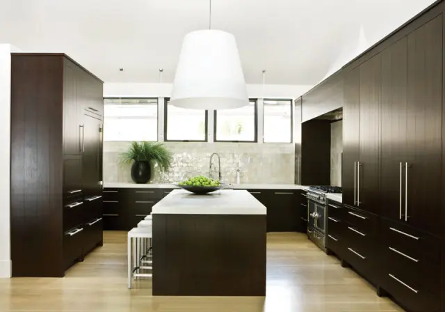 Dark wood kitchen with white quartz island, stainless steel appliances, and a textured tile backsplash.