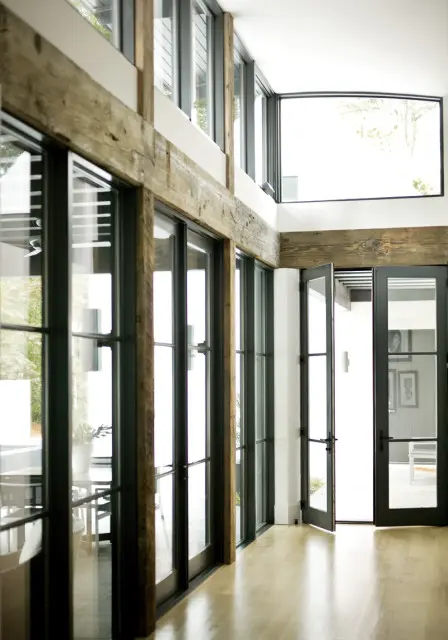 Modern interior with large glass doors and windows, exposed wooden beams, and light wood floors.