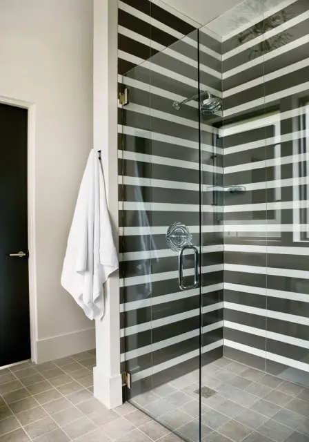 Modern bathroom with a glass-enclosed shower featuring black and white horizontal striped tile, chrome fixtures, and a white towel hanging on a nearby hook.