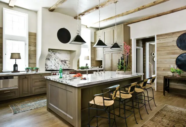 Rustic kitchen with marble island, wood plank walls, exposed beams, and pendant lighting. A range is visible behind the island.