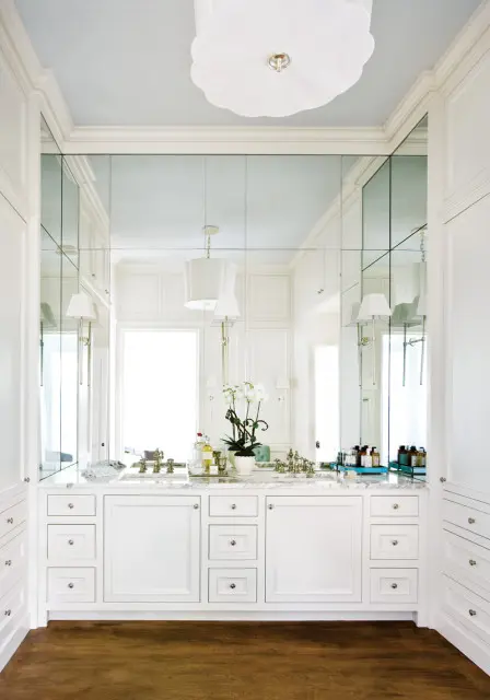 White bathroom with double vanity, marble countertop, mirrored wall, and built-in cabinetry.