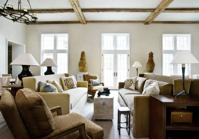 Living room with two tan sofas, upholstered armchairs, a wooden trunk coffee table, and exposed wooden ceiling beams.