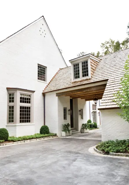 White brick house with a gabled roof, dormer windows, and a covered entryway with a wooden beam.