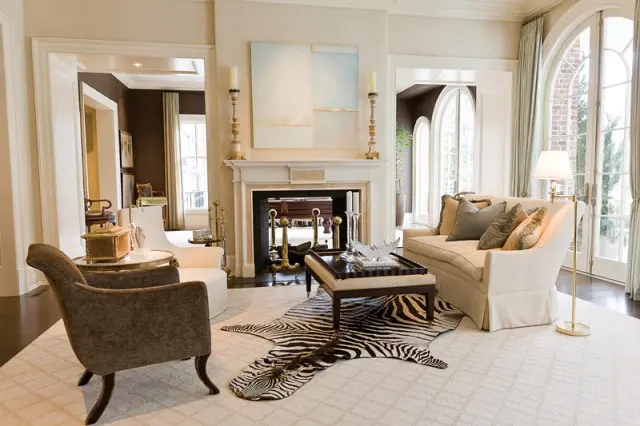 Living room with a cream sofa, brown armchair, zebra rug, fireplace with abstract art, and arched French doors.