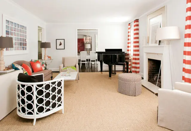 Living room with a black grand piano, fireplace, white armchair, and red and white striped curtains. A dining room is visible through an open doorway.