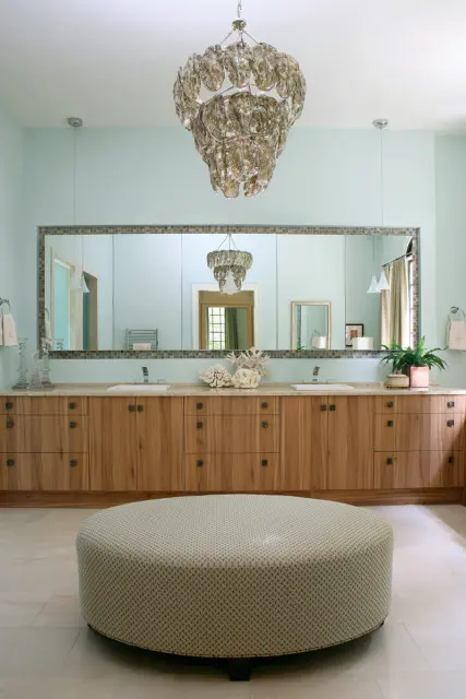 Master bathroom with light blue walls, a long wooden vanity with two sinks, a large mirror, and a decorative chandelier.