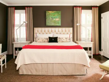 Master bedroom with dark brown walls, a tufted cream headboard, cream bedding with a red throw, and beige curtains with red trim.