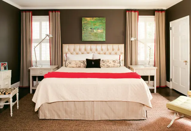 Master bedroom with dark brown walls, a tufted cream headboard, cream bedding with a red throw, and beige curtains with red trim.