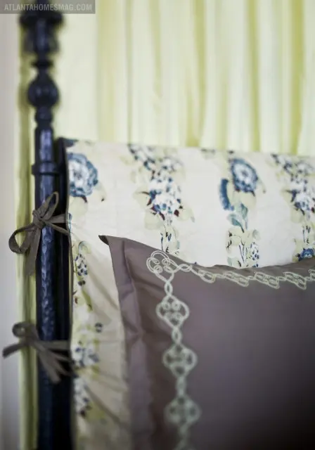 Close-up of a dark-colored bed frame with floral patterned bedding and a taupe pillow with light green embroidery.