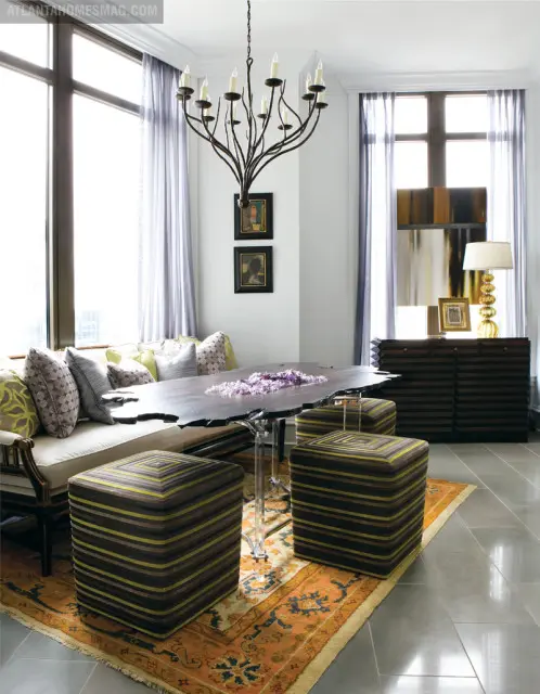 Dining room with a live-edge wood table, acrylic pedestal base, striped ottomans, built-in banquette seating, and a wrought iron chandelier.